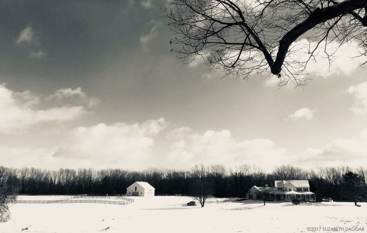 black and white photograph of a farm house in a snowy field