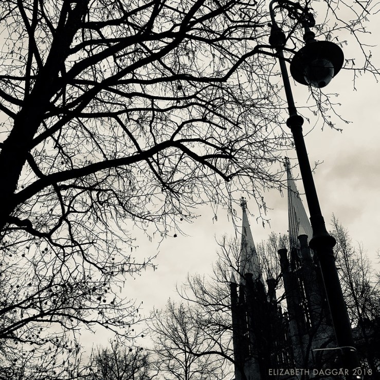 b&w photo of a lamp post, tree branches and spires in Berlin